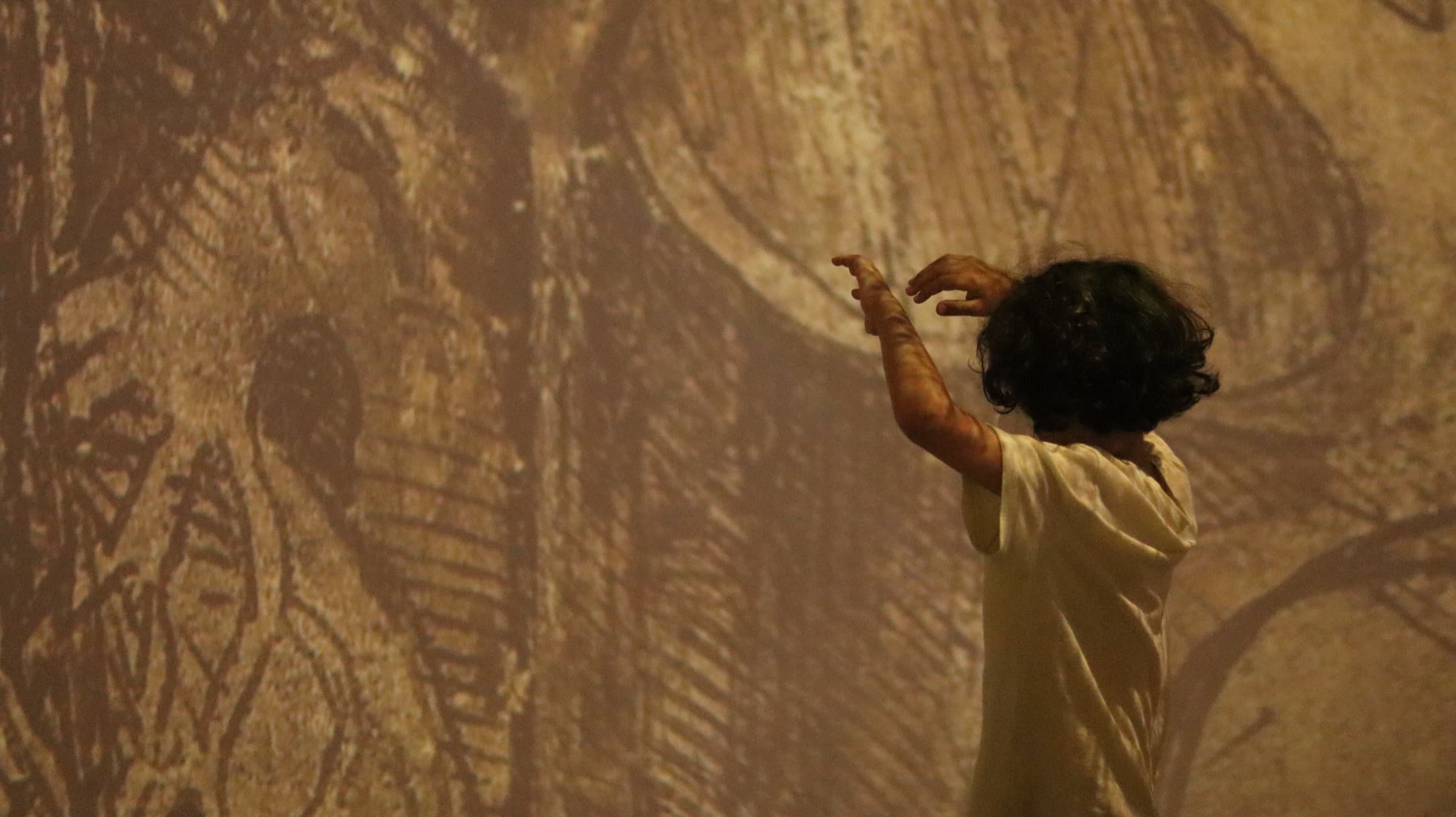 A child reaching toward projected ancient wall art in a dark room